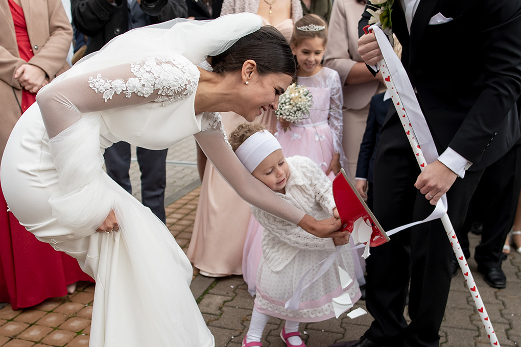 Dievčatko s lopatkou pomáha neveste pozametať črepy taniera