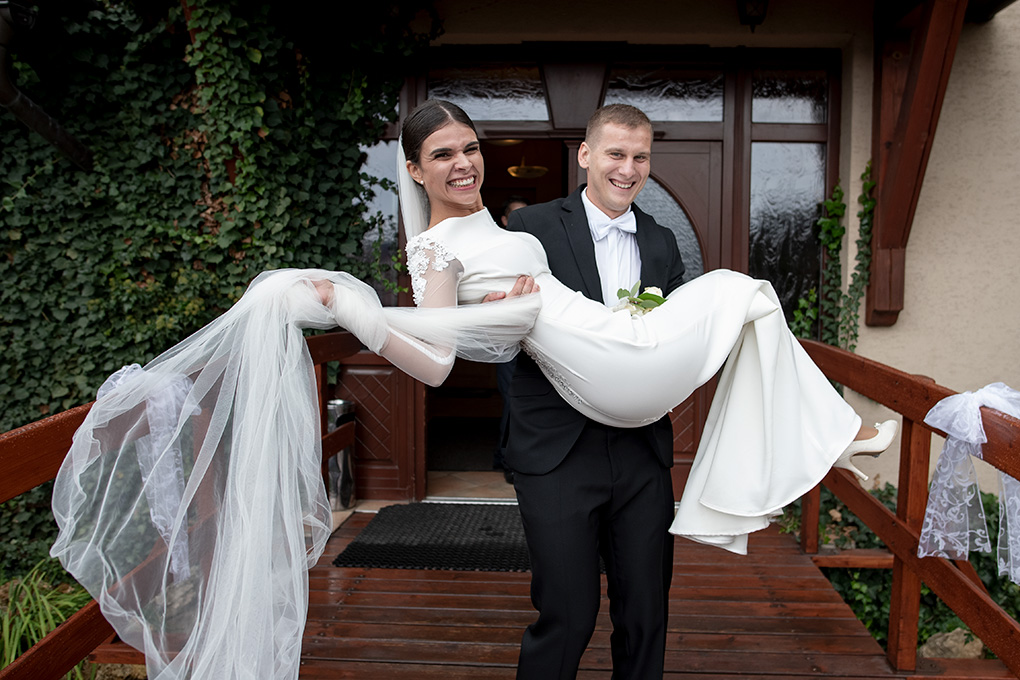 Ženích prenáša usmiatu nevestu cez drevený mostík