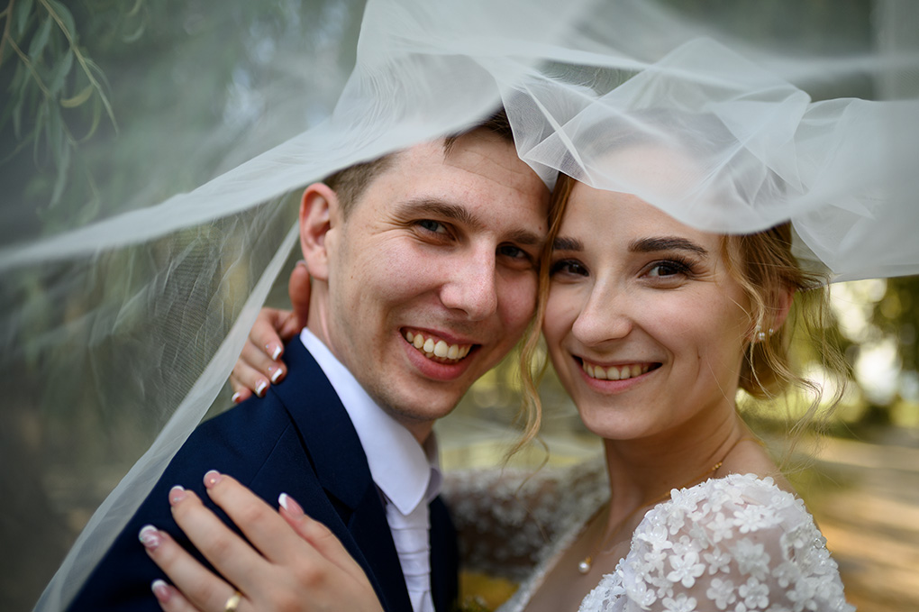 Detailný záber na zamilovaný pár schovaný pod dlhým čipkovaným závojom.