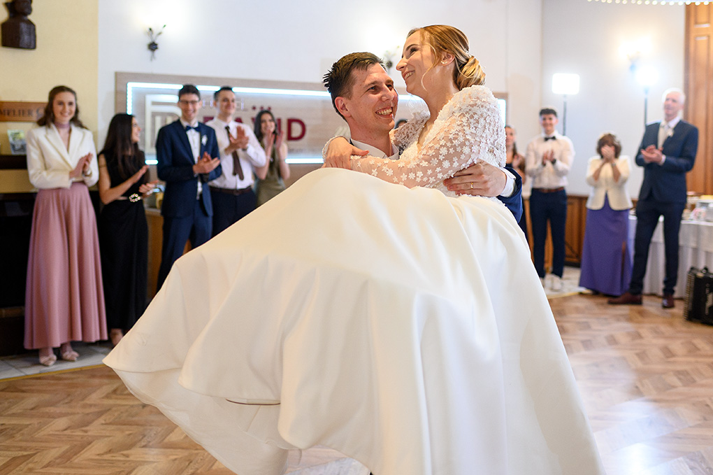 Ženích s úsmevom drží a točí nevestu v náručí počas tanečnej choreografie.