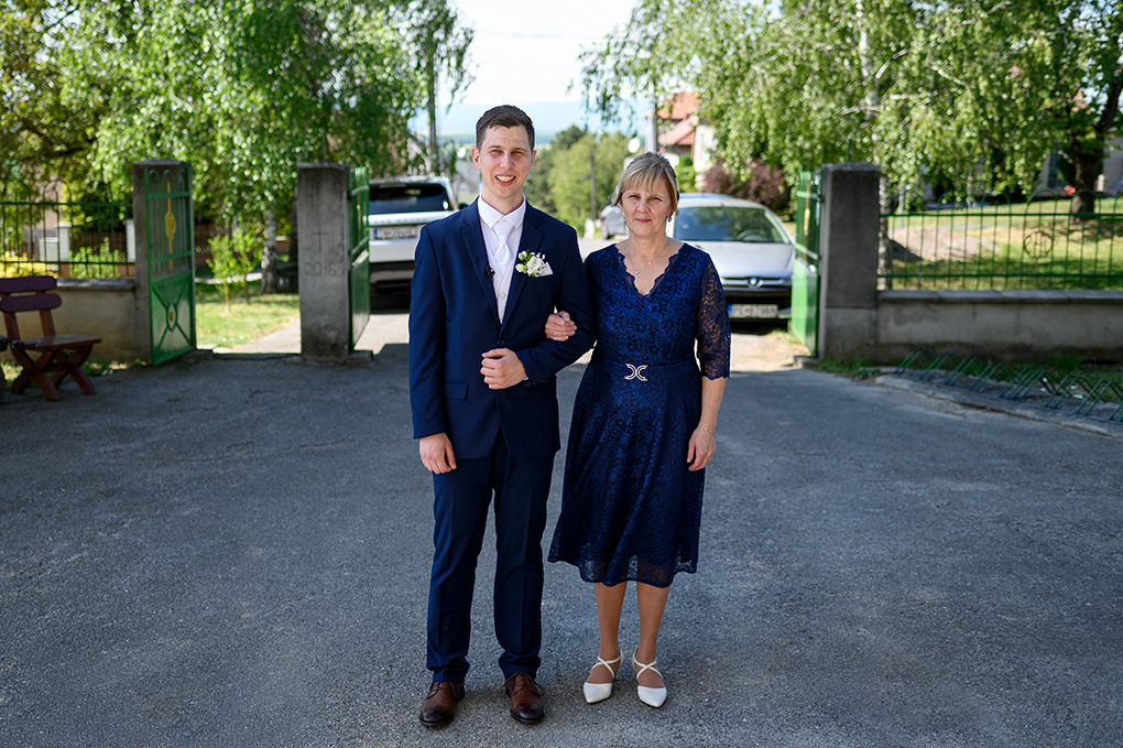 Ženích a svadobná mama stoja pred vstupnou bránou na dvore.