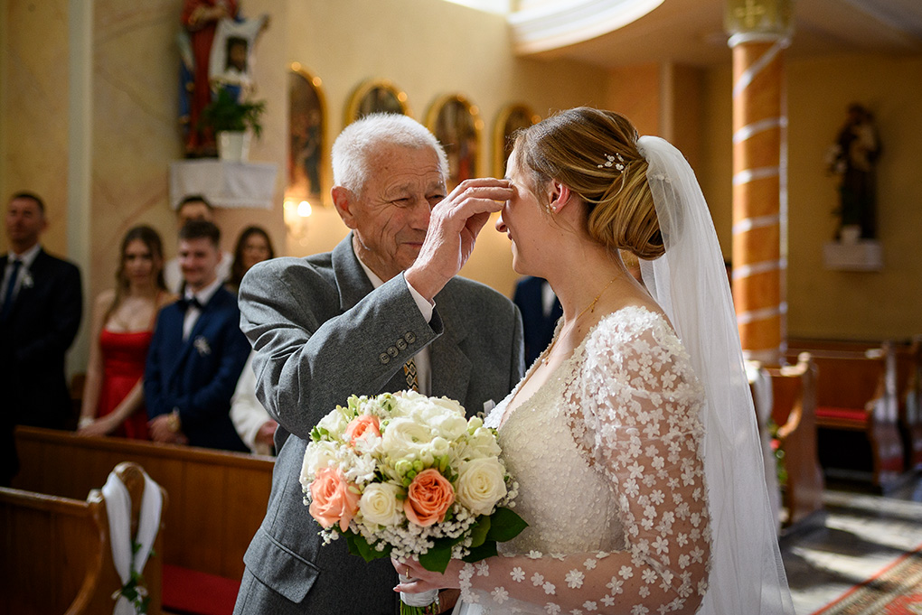 Svadobný otec utiera neveste slzu spod oka v kostolnej uličke.
