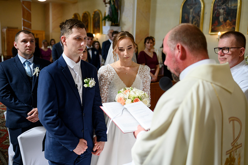 Ženích a nevesta počúvajú kňaza pred oltárom počas obradu.