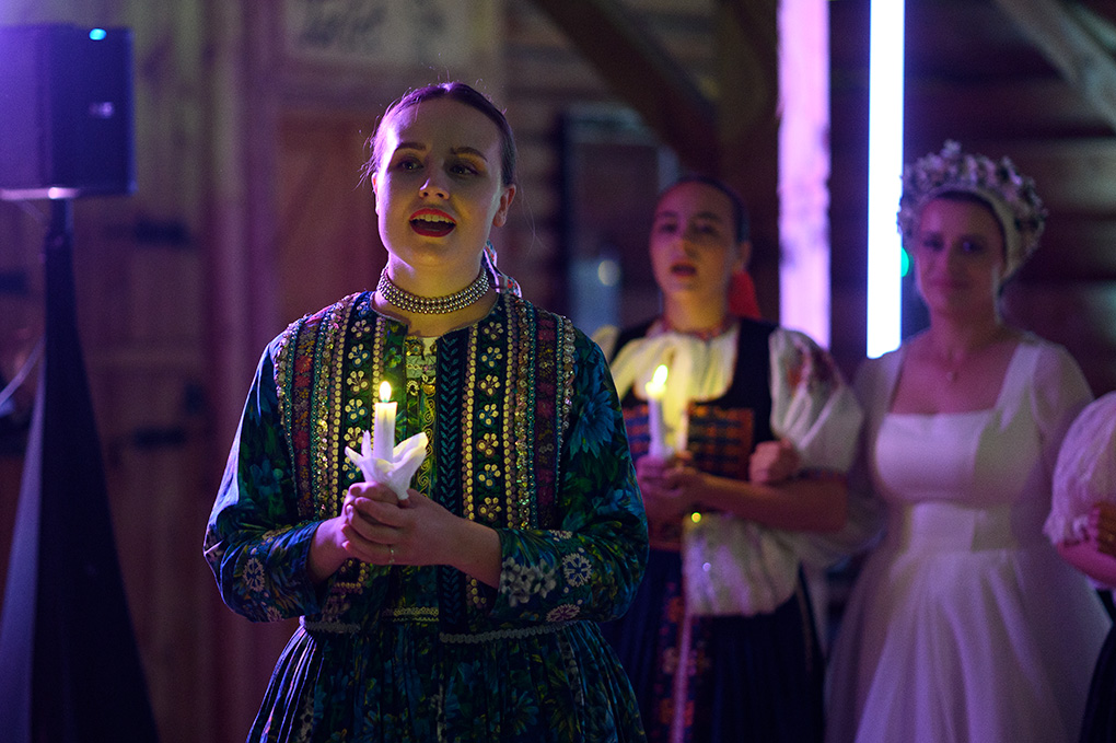 Členka folklórneho súboru drží zapálenú sviečku počas začiatku odčepčenia nevesty.