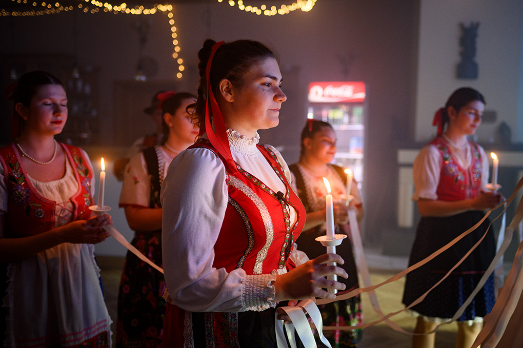 Členky folklórneho súboru držiace zapálené sviečky počas svadobného obradu.