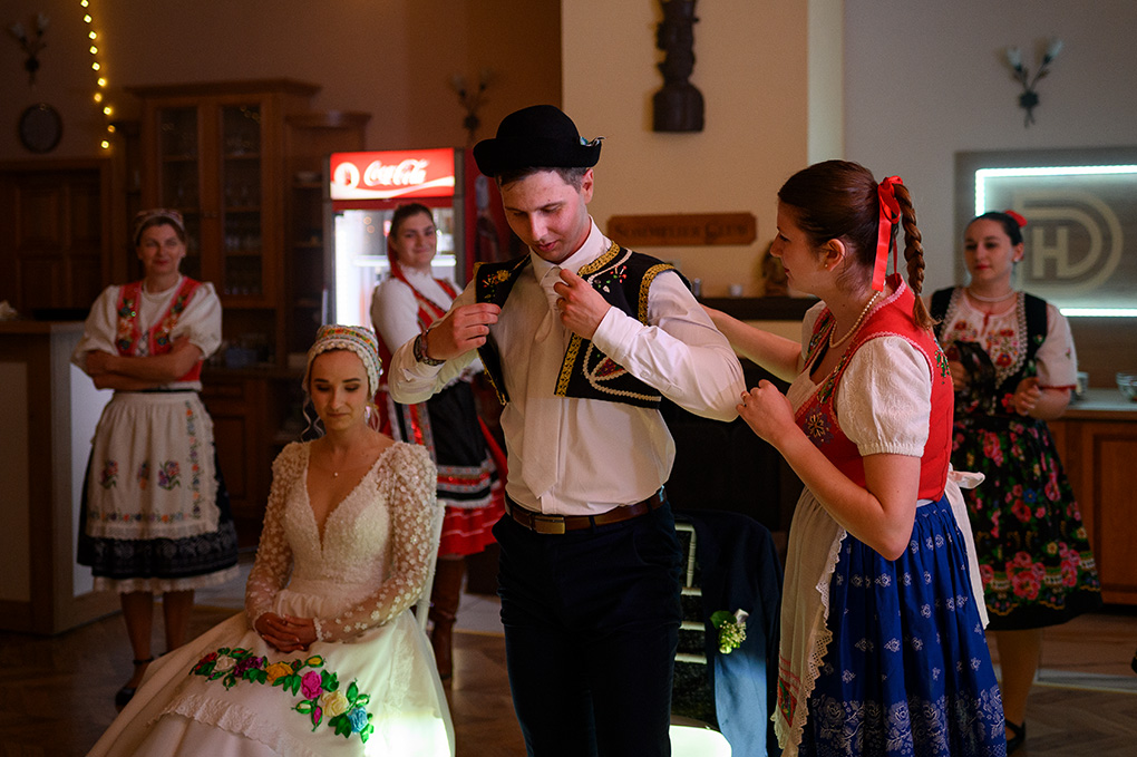 Členka FS Vienok oblieka ženíchovi krojovanú vestu a klobúk, kým nevesta má založený čepiec.