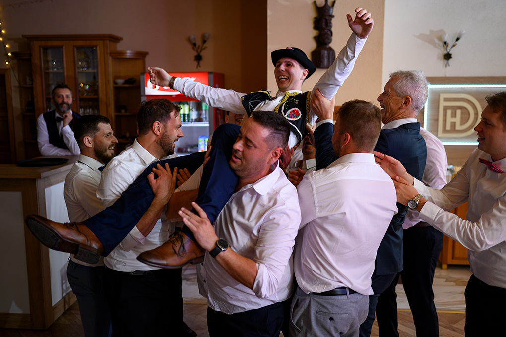 Muži dvíhajú ženícha na ruky počas vykrúcanky po čepčení.