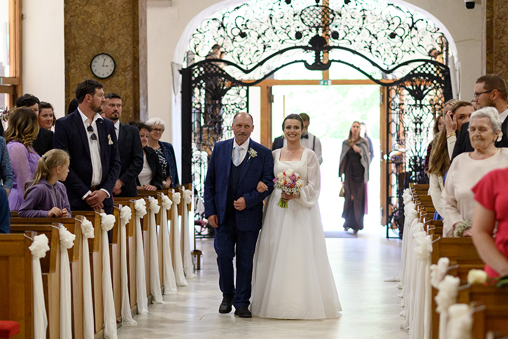 Nevesta prichádza kostolnou uličkou so svadobnou kyticou smerom k oltáru.