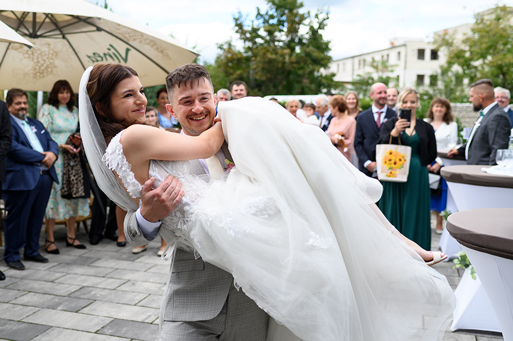 Ženích prenáša nevestu cez prah pred hosťami.