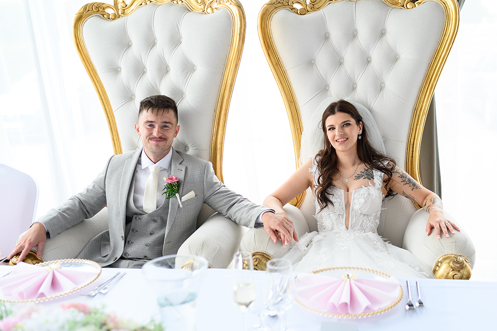Novomanželia v kráľovských kreslách za hlavným stolom.