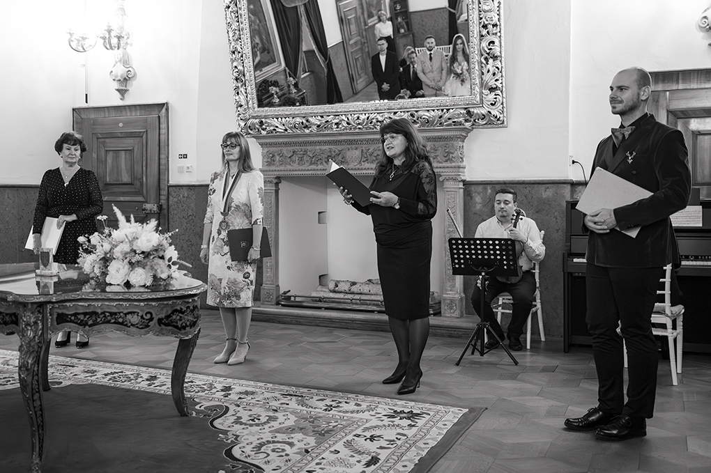 Oddávajúci v sále Pohľad na oddávajúcich a hudobníkov v historickom interiéri.