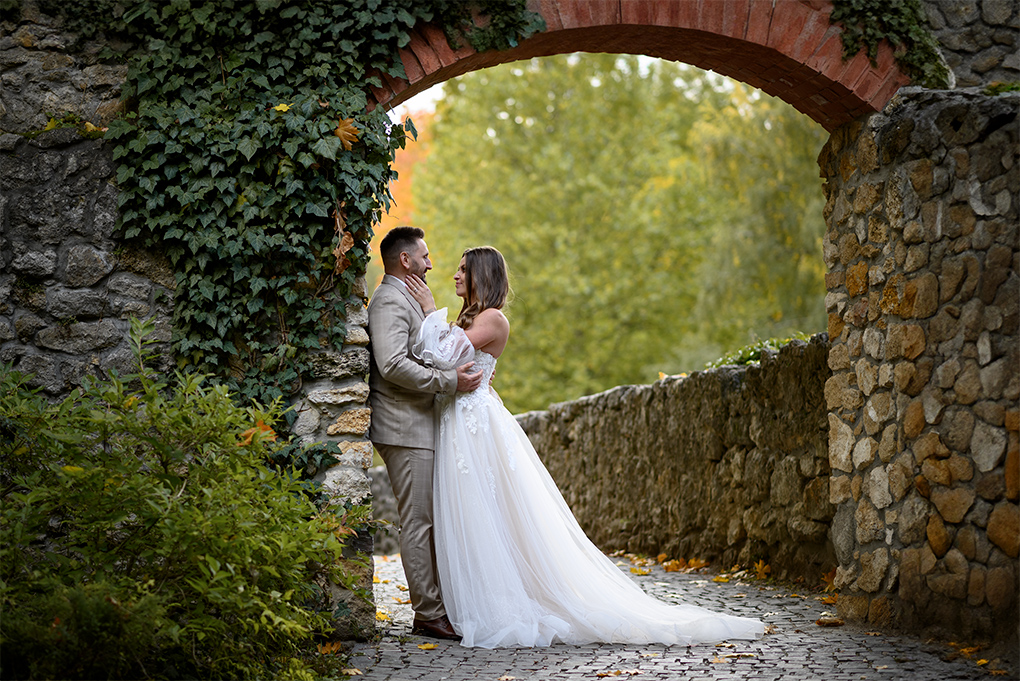 Pod oblúkom Novomanželia stoja pod tehlovým oblúkom v parku.