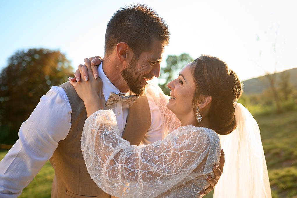 Detailný záber na usmievajúcich sa novomanželov v protisvetle počas západu slnka.