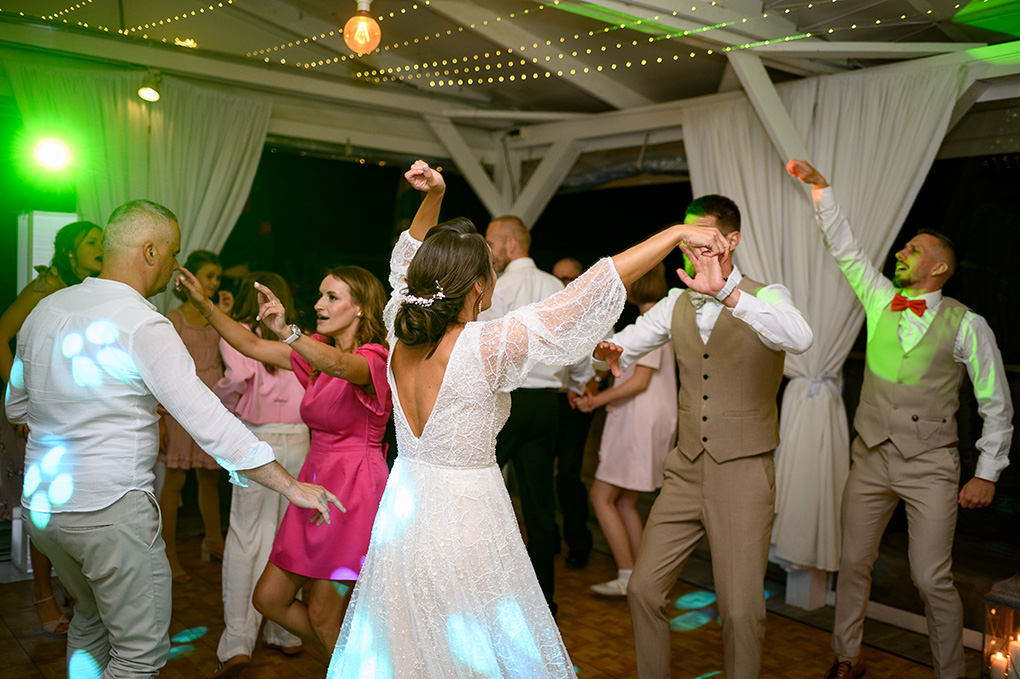 Mladomanželia a hostia si užívajú večernú svadobnú párty pod svetelnými reťazami.