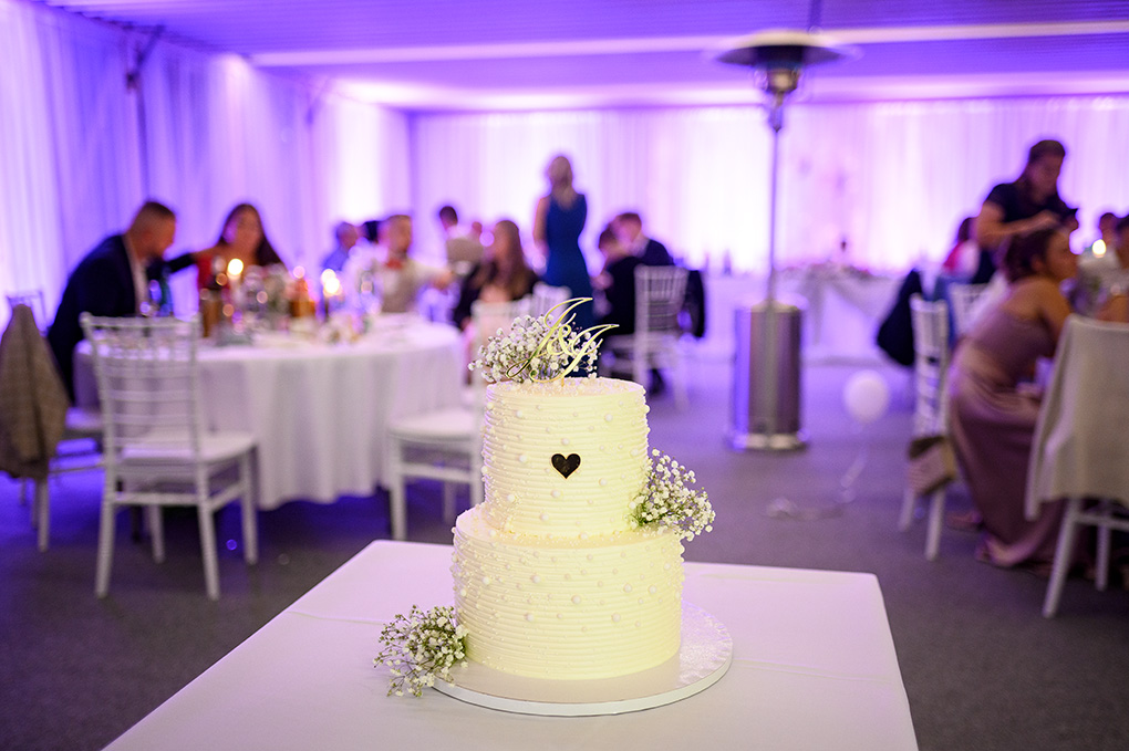 Elegantná biela svadobná torta s jemným zdobením a kvetmi pripravená na krájanie.