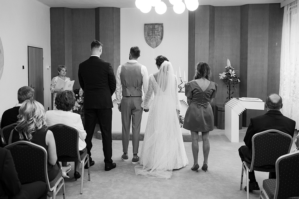 Pohľad na svadobný obrad v interiéri Obecného úradu Veľké Úľany so štátnym znakom na stene.