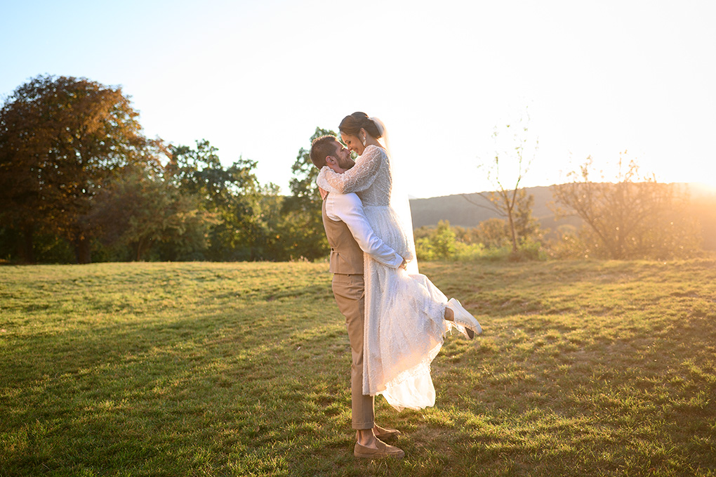 Ženích zdvíha nevestu v náručí na rozkvitnutej lúke pred historickým kláštorom.