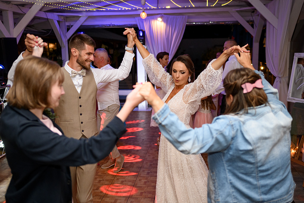 Svadobčania sa držia za ruky a tancujú v kruhu spolu s novomanželmi.