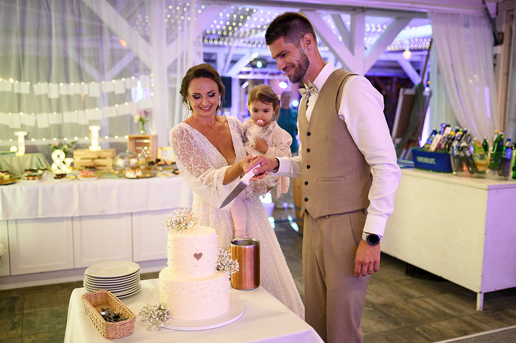 Nevesta a ženích v béžovej veste sa usmievajú pri krájaní svadobnej torty v Kerkira Pube.