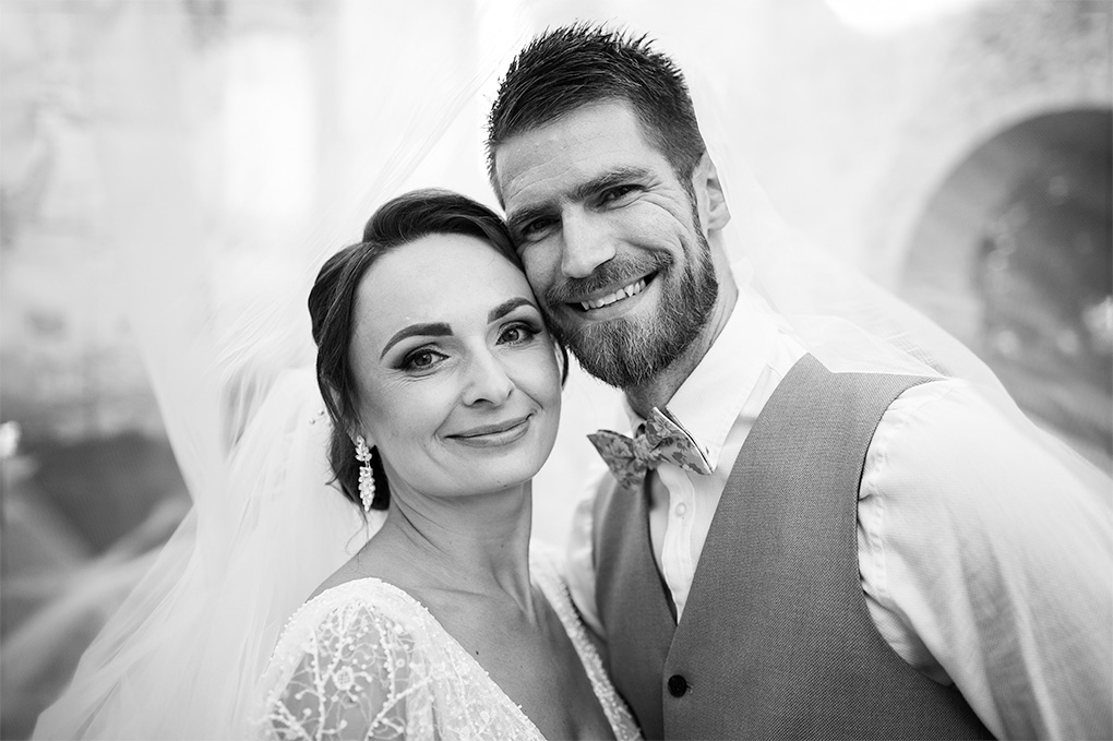 Šťastný svadobný pár pózuje pod priesvitným závojom v areáli kláštora Katarínka.