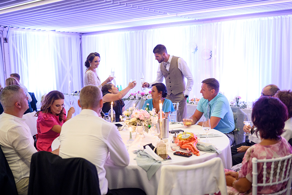 Novomanželia si pripíjajú so svojimi hosťami pri slávnostne prestretom stole.