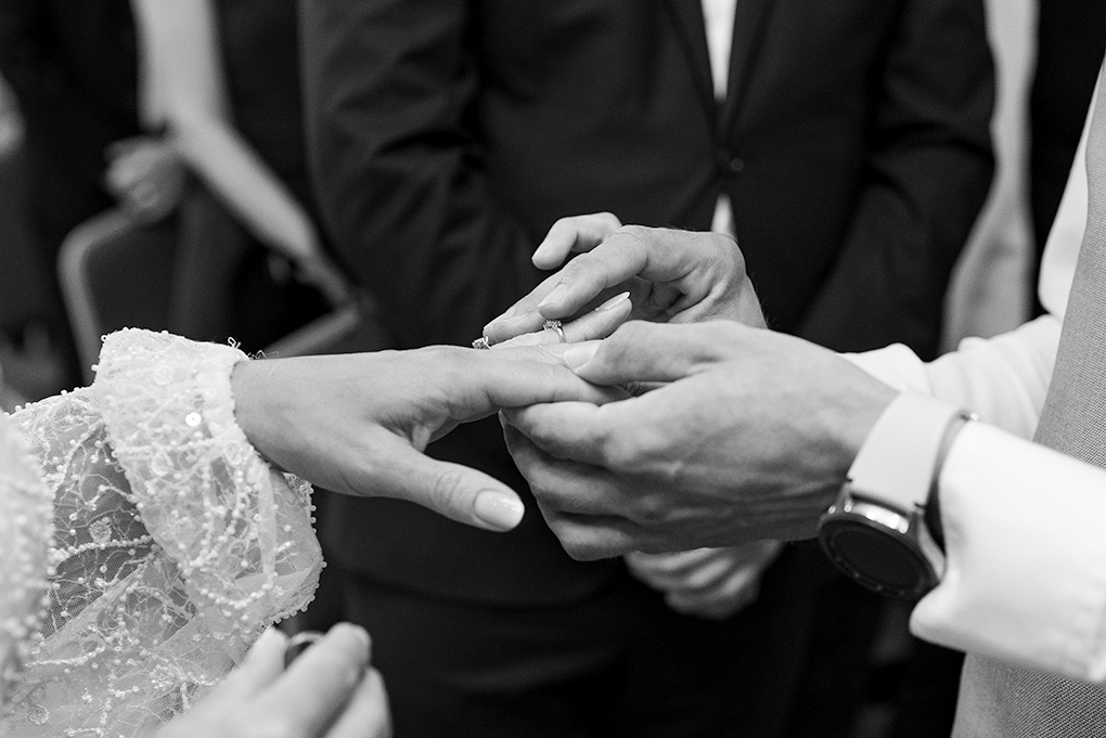 Ženích navlieka prsteň neveste, svedkovia sa prizerajú v pozadí.