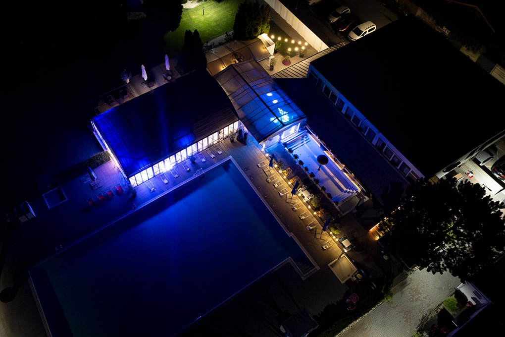 Nočný pohľad z dronu na vysvietený areál Kerkira Pub s bazénom vo Veľkých Úľanoch.