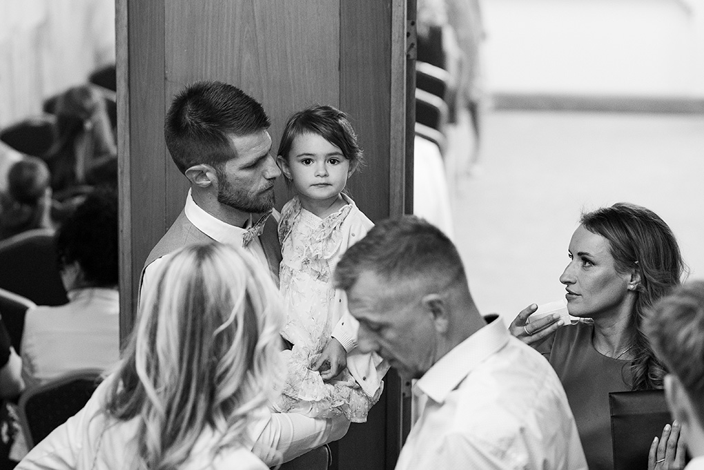 Ženích drží v náručí malé dievčatko počas gratulácií, emotívny moment.